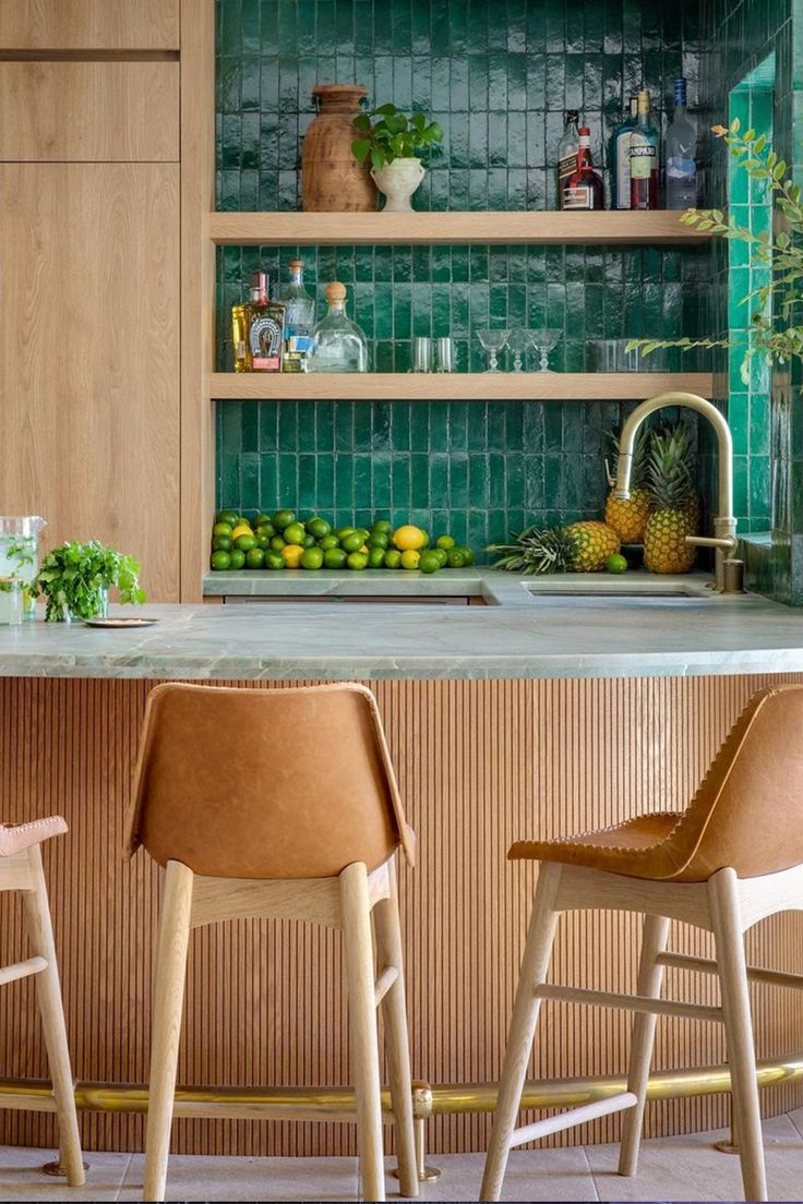 A kitchen features a glistening green zellige wall with wooden cabinetry and tan leather counter stools. Roof Tiles Design, Tommy Bahama Kitchen, Zia Tile, Moroccan Architecture, Tiles Design, Roof Tiles, Kitchen Tile, Architecture And Design, Outdoor Kitchen Design