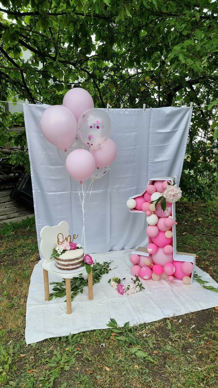 a table topped with balloons and a number one cake sitting on top of a field