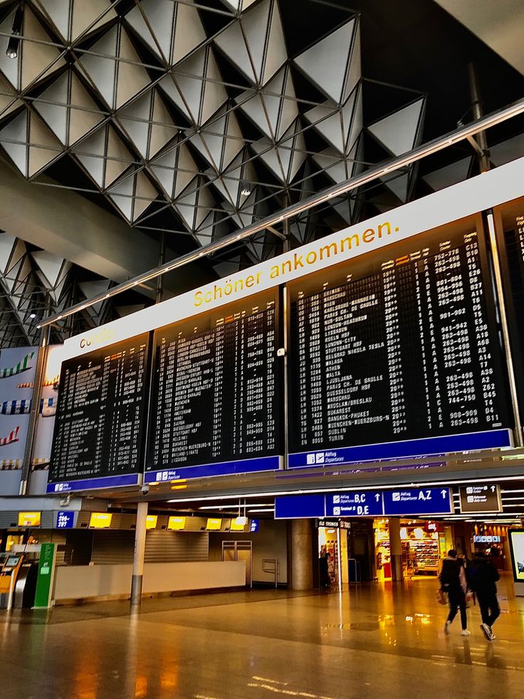 people are walking through an airport terminal with their luggage and check - in boards on the wall