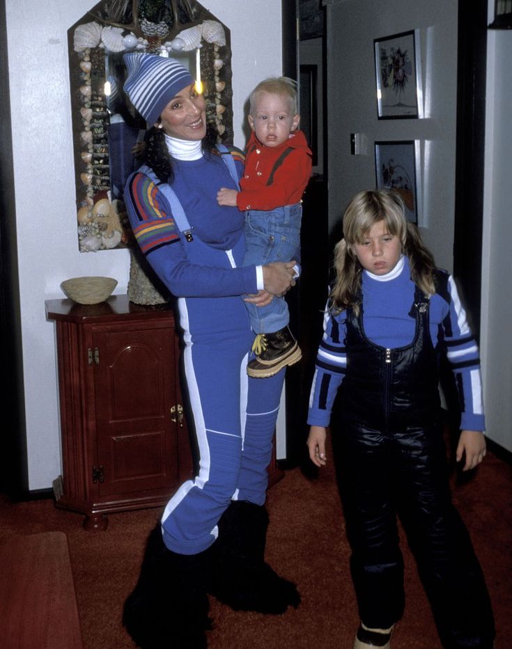 a woman holding a child in her arms while standing next to two other people wearing space suits