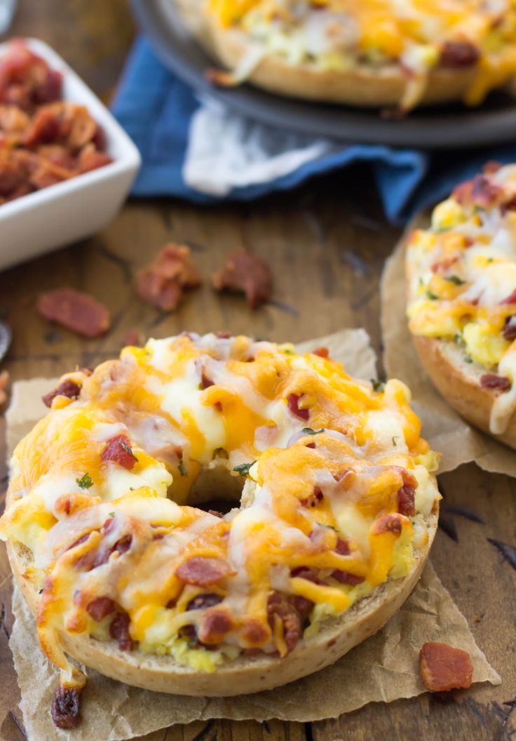 two bagels covered in cheese and bacon sitting on top of a wooden table