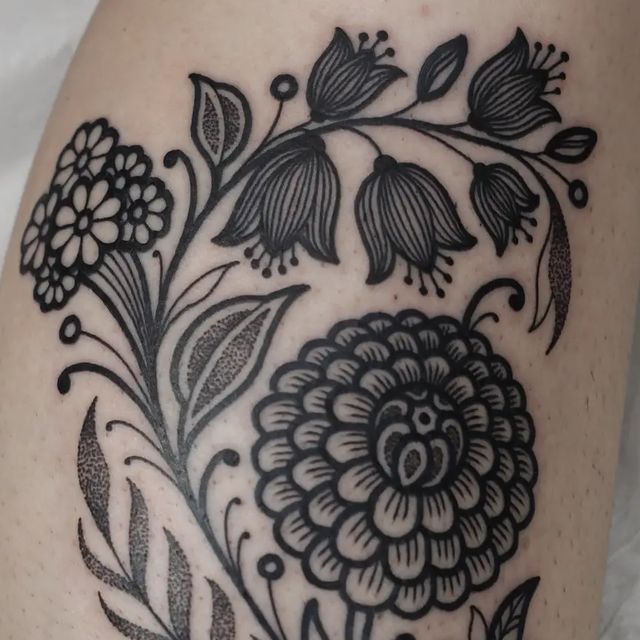 a black and white flower tattoo design on the right side of the leg, with leaves and flowers around it