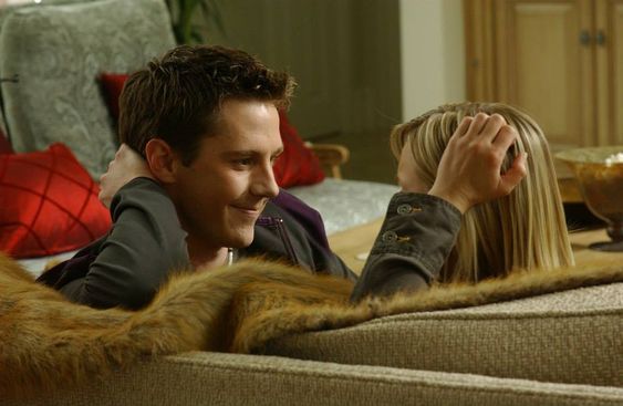 a man and woman sitting on a couch looking at each other's eyes,