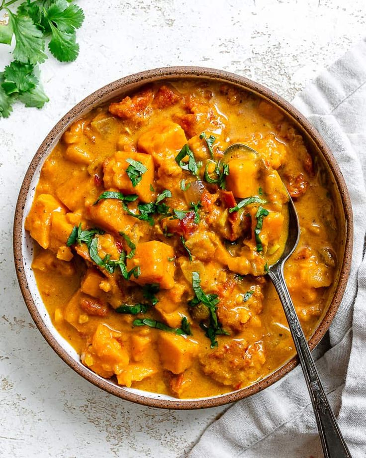 a bowl filled with chicken and spinach stew next to a spoon on top of a napkin