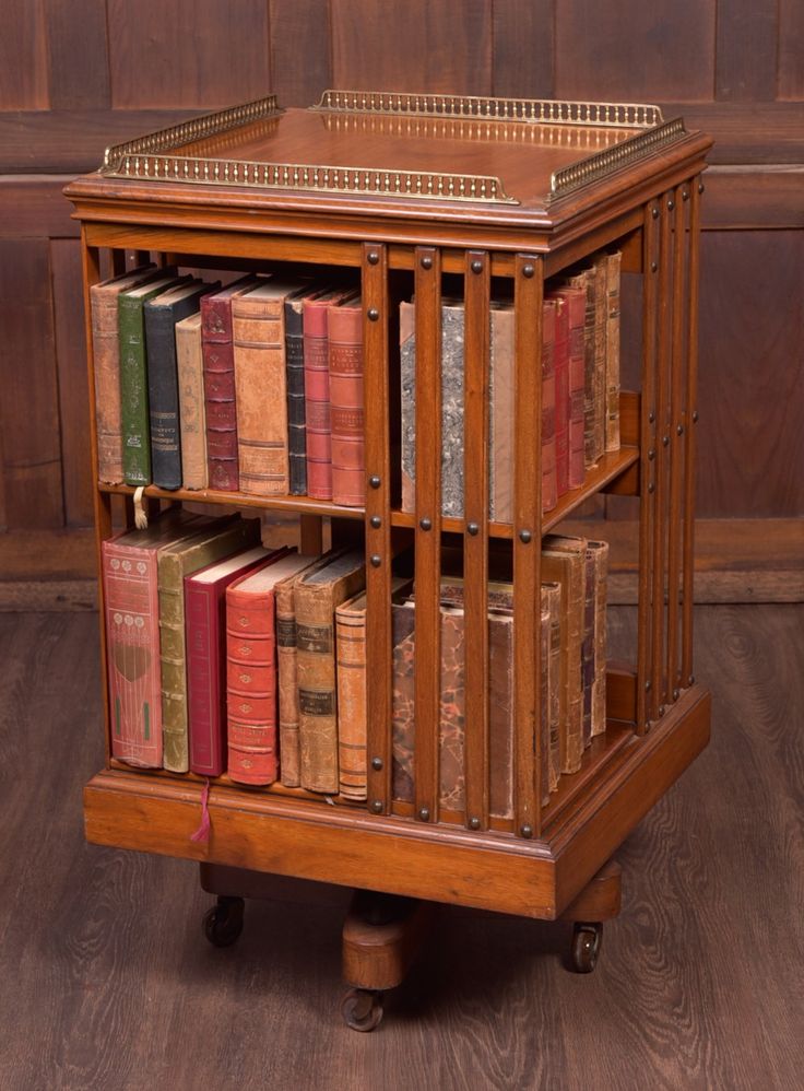 an old wooden book shelf with many books on it's sides and wheels, in front of a wood paneled wall