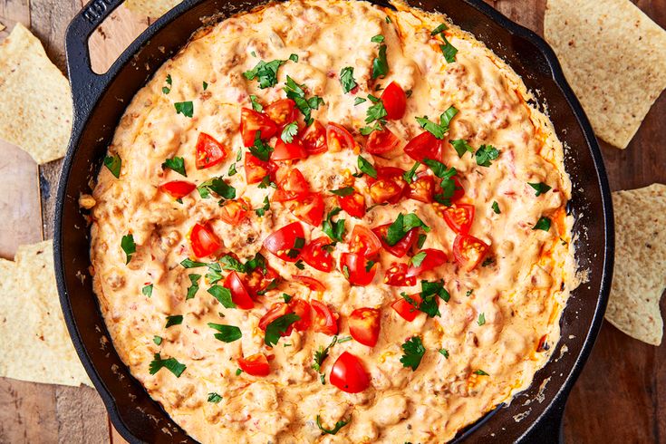 a pizza in a pan with tomatoes, cheese and tortilla chips on the side