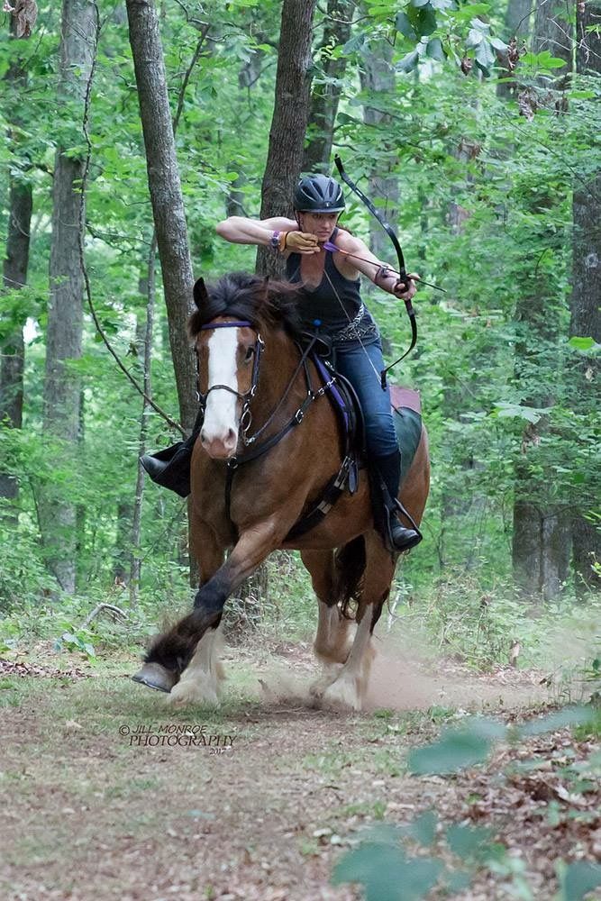 a woman riding on the back of a brown horse through a forest