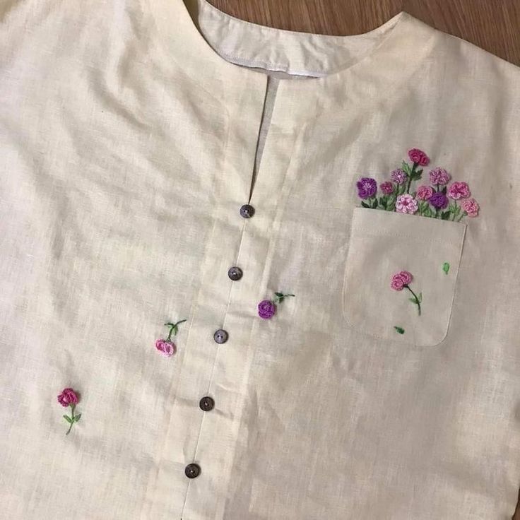 a white shirt with pink and purple flowers embroidered on the chest, along with black buttons