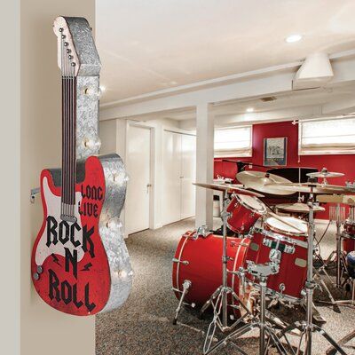 a red guitar hanging from the side of a wall in a room with drums and stools