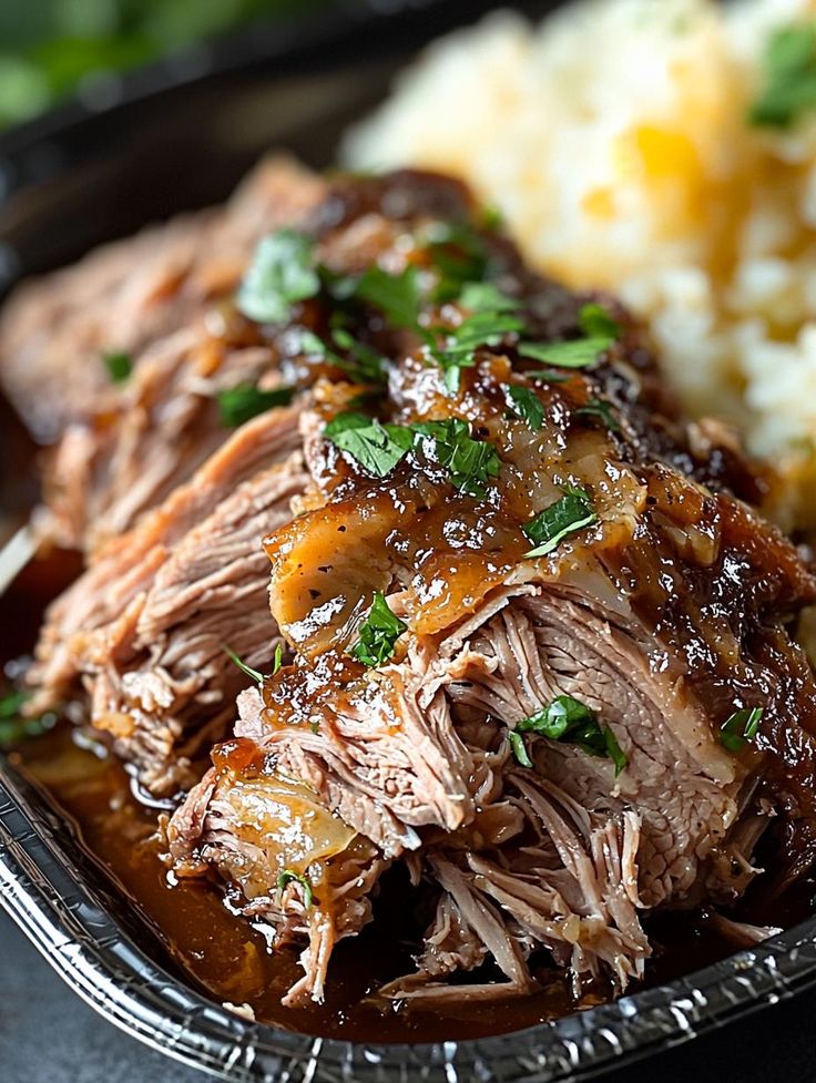 a plate with meat, mashed potatoes and gravy on it next to green garnish