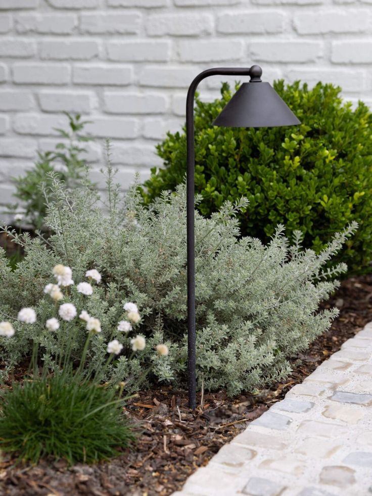 a black lamp sitting in the middle of a flower bed next to a brick wall