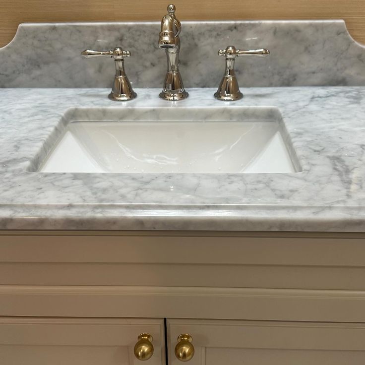 a bathroom sink with two faucets on the top and marble countertop above it