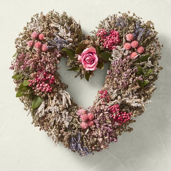 a heart shaped wreath with pink flowers and greenery on the inside, hanging on a wall