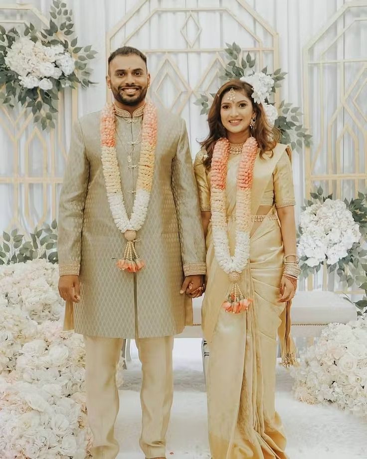 a man and woman standing next to each other in front of a flower covered wall