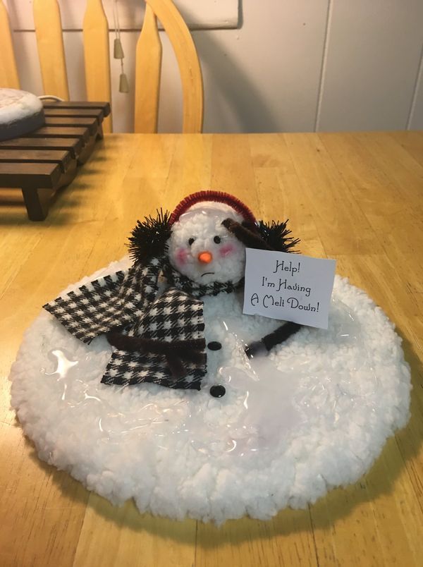 a snowman with a hat and scarf sitting on top of a wooden table next to a sign