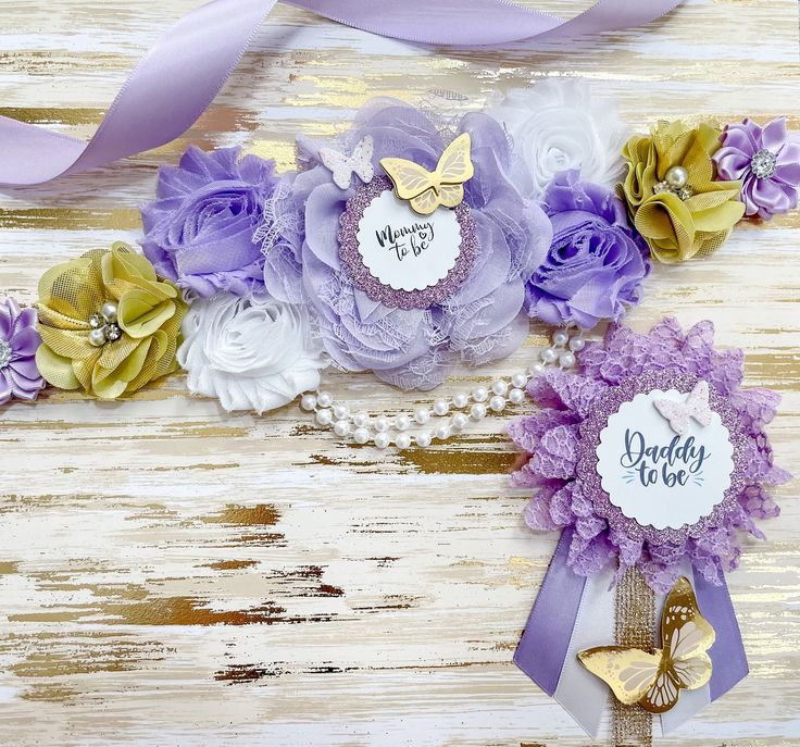 two purple and gold flower bouquets with name tags attached to them on a white wooden background