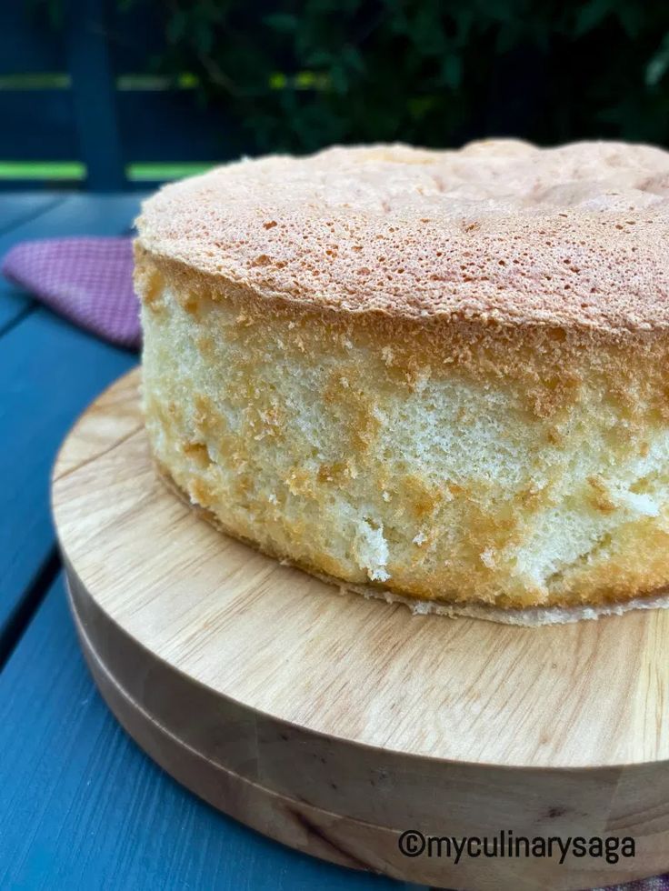 a round cake sitting on top of a wooden cutting board next to a blue table