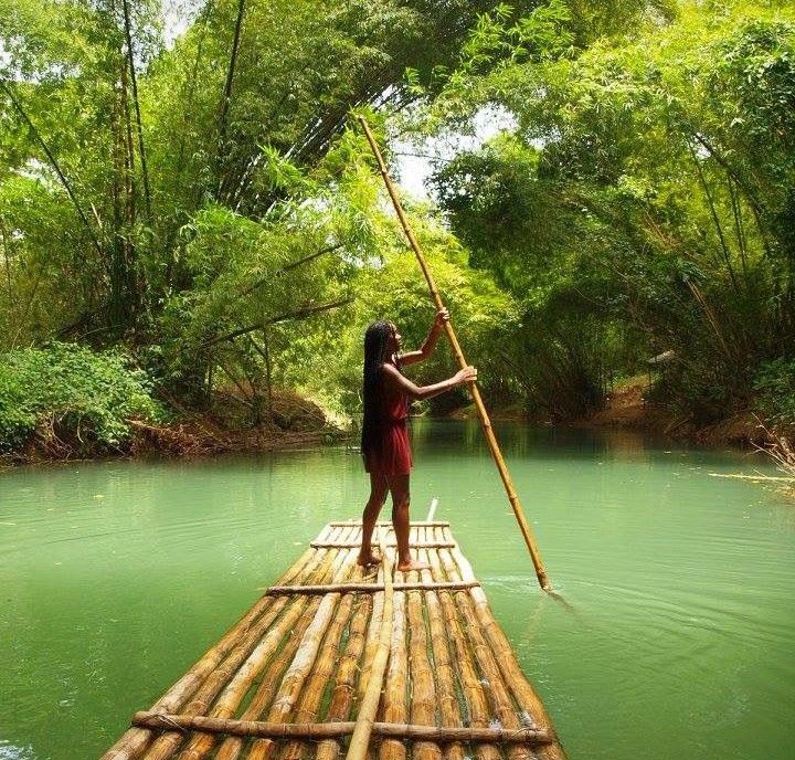 a woman standing on top of a bamboo raft in the middle of a river surrounded by trees