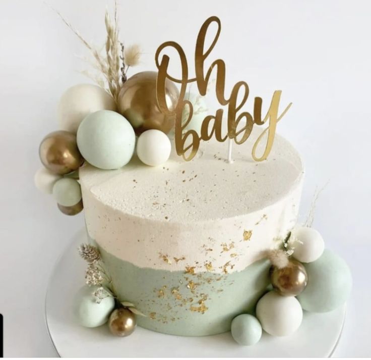 a cake with gold and white frosting on it that says oh baby next to some ornaments