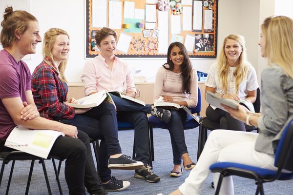 a group of people sitting in chairs talking to each other with books on their laps