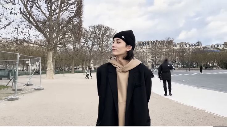 a woman standing in the middle of a park wearing a black coat and scarf with her eyes closed