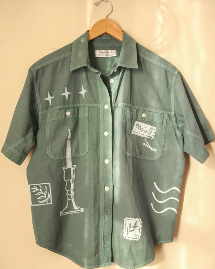 a green button up shirt with stickers on the front and back pockets, hanging from a hanger