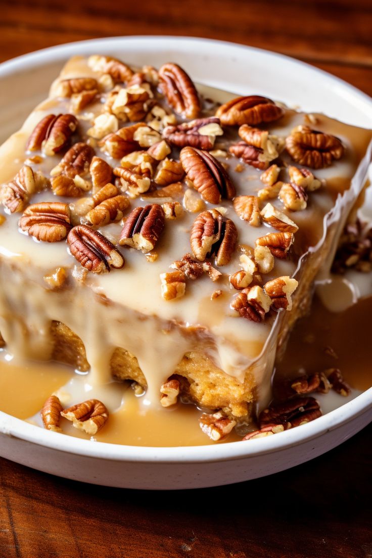 a white plate topped with cake covered in frosting and pecan toppings on top of a wooden table