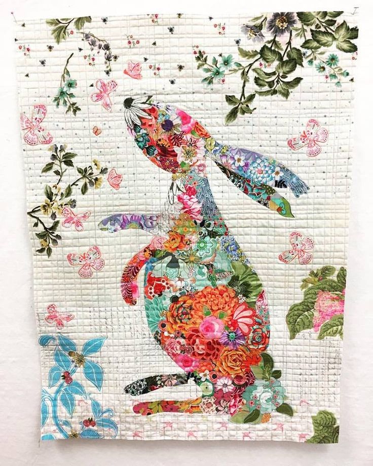 a quilted rabbit with flowers and leaves on it's back, sitting in front of