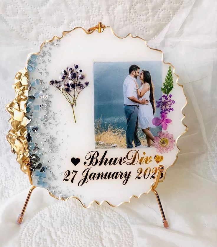 a photo frame with a couple holding each other and flowers in the middle on a white table cloth