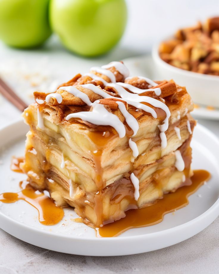 a white plate topped with dessert covered in icing and caramel sauce next to two green apples