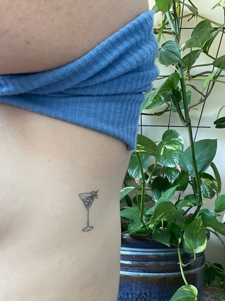 a woman's stomach with a small martini glass tattoo on her left side ribcage