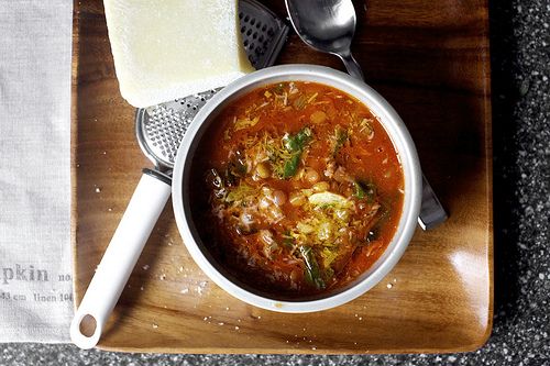 a bowl of soup on a wooden tray with two spoons next to it and cheese