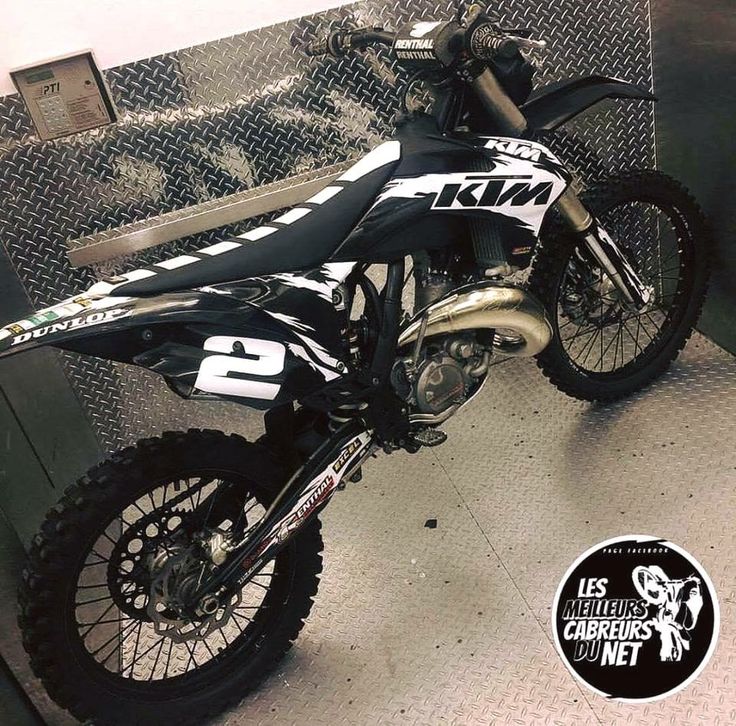 a black and white dirt bike sitting on top of a metal floor next to a chain link fence