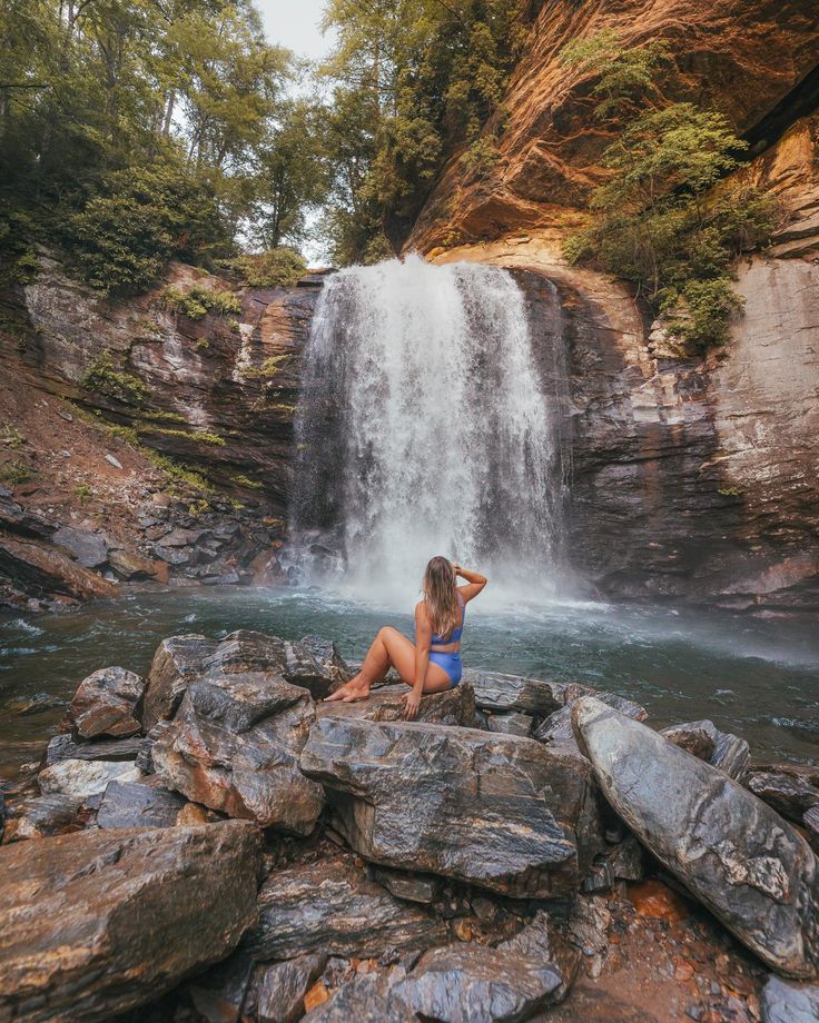 a woman sitting on rocks in front of a waterfall