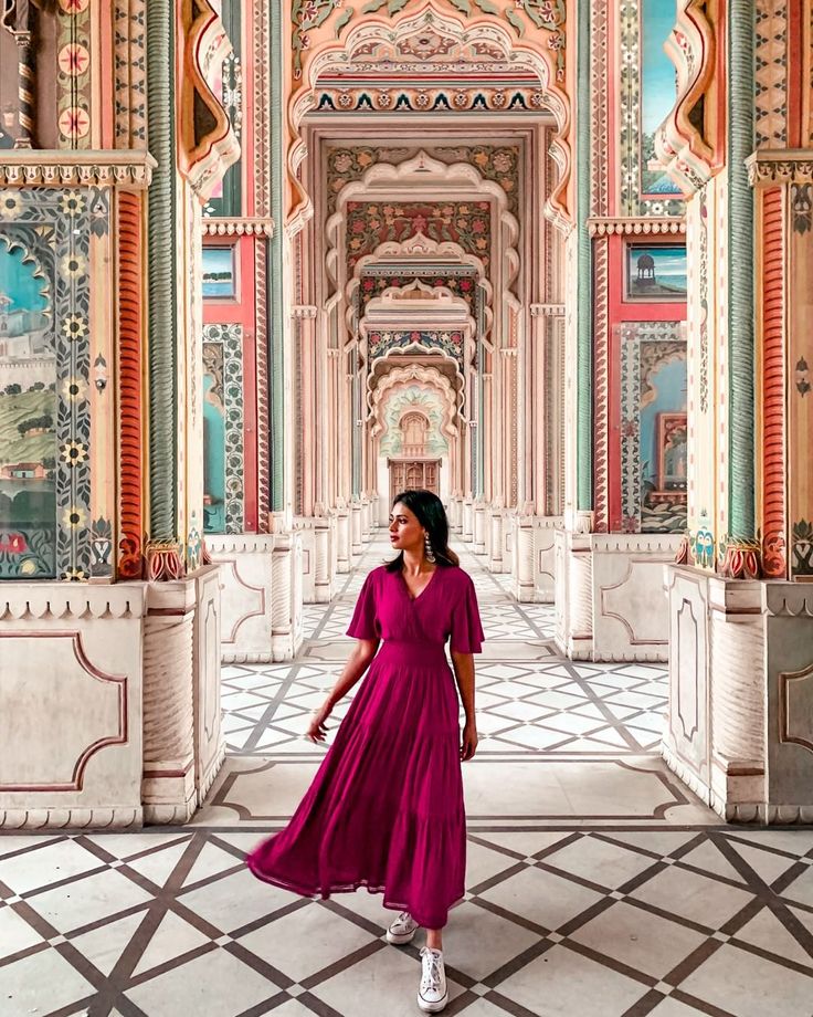 a woman in a pink dress is walking through an ornate building with columns and arches