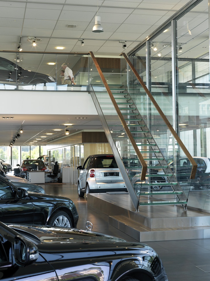 a car showroom filled with lots of cars and people walking up to the stairs