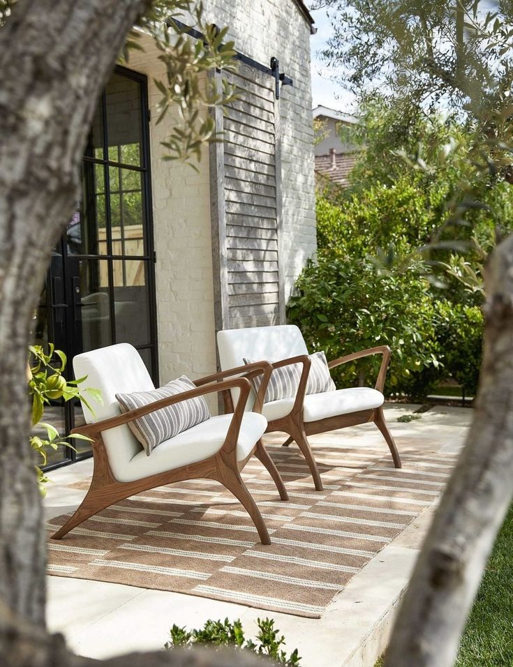 two white chairs sitting on top of a wooden deck next to a tree and building