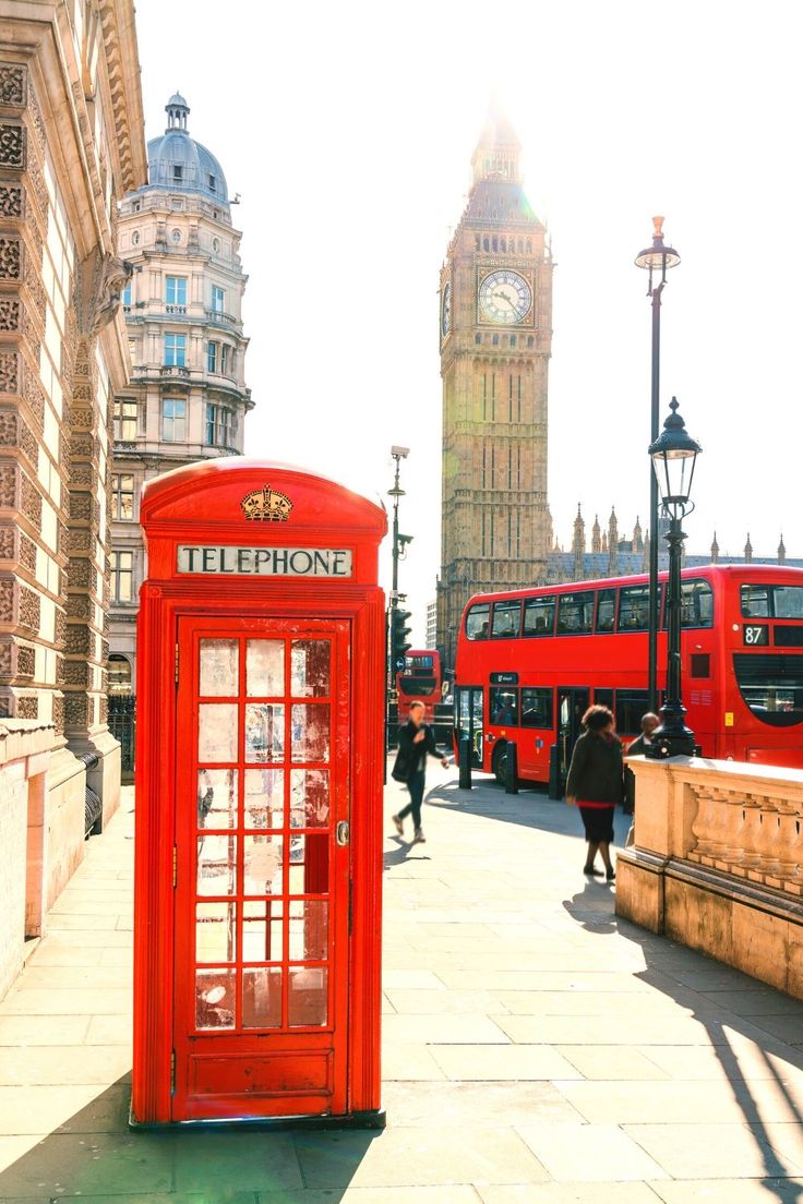 a red phone booth sitting on the side of a road next to a tall clock tower