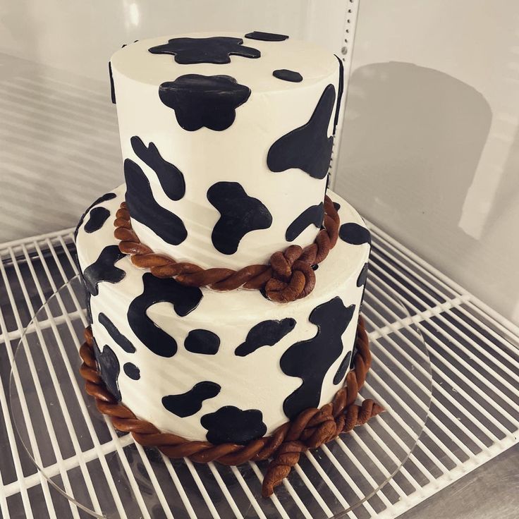 a three tiered cake decorated with black and white cow print icing on a cooling rack