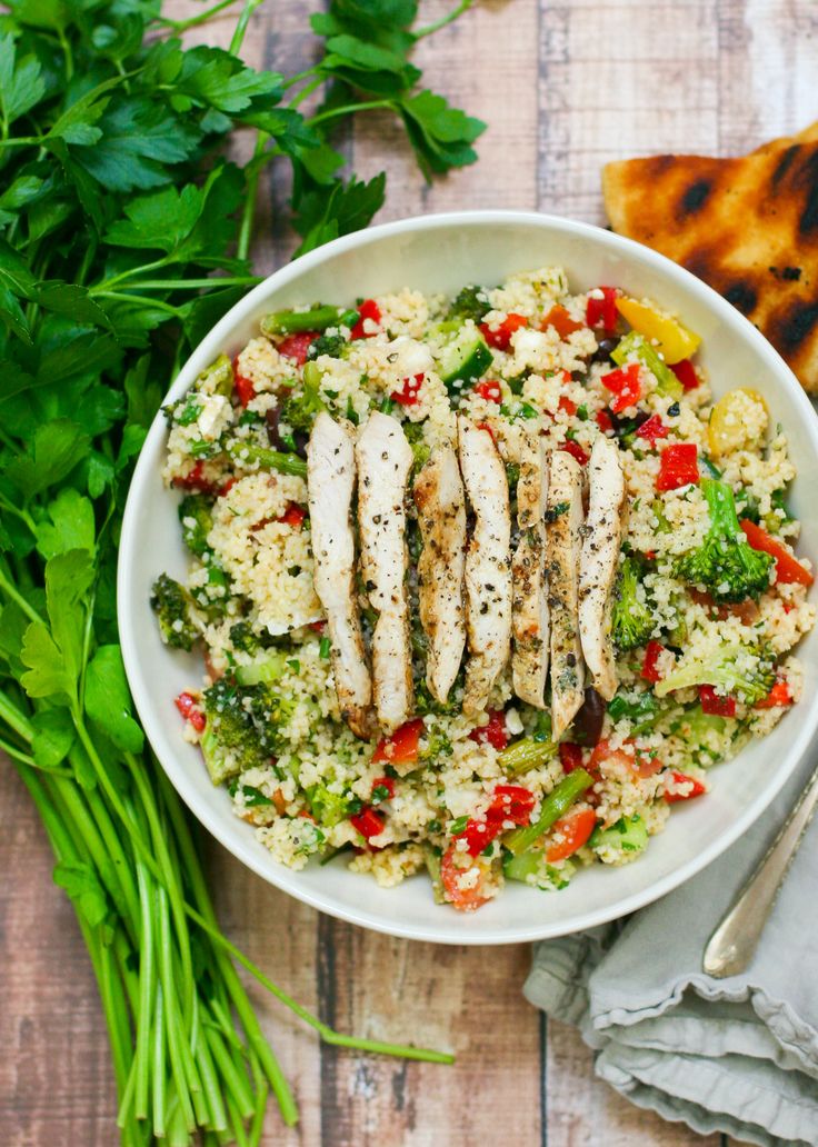 a white bowl filled with chicken, rice and veggies on top of a wooden table