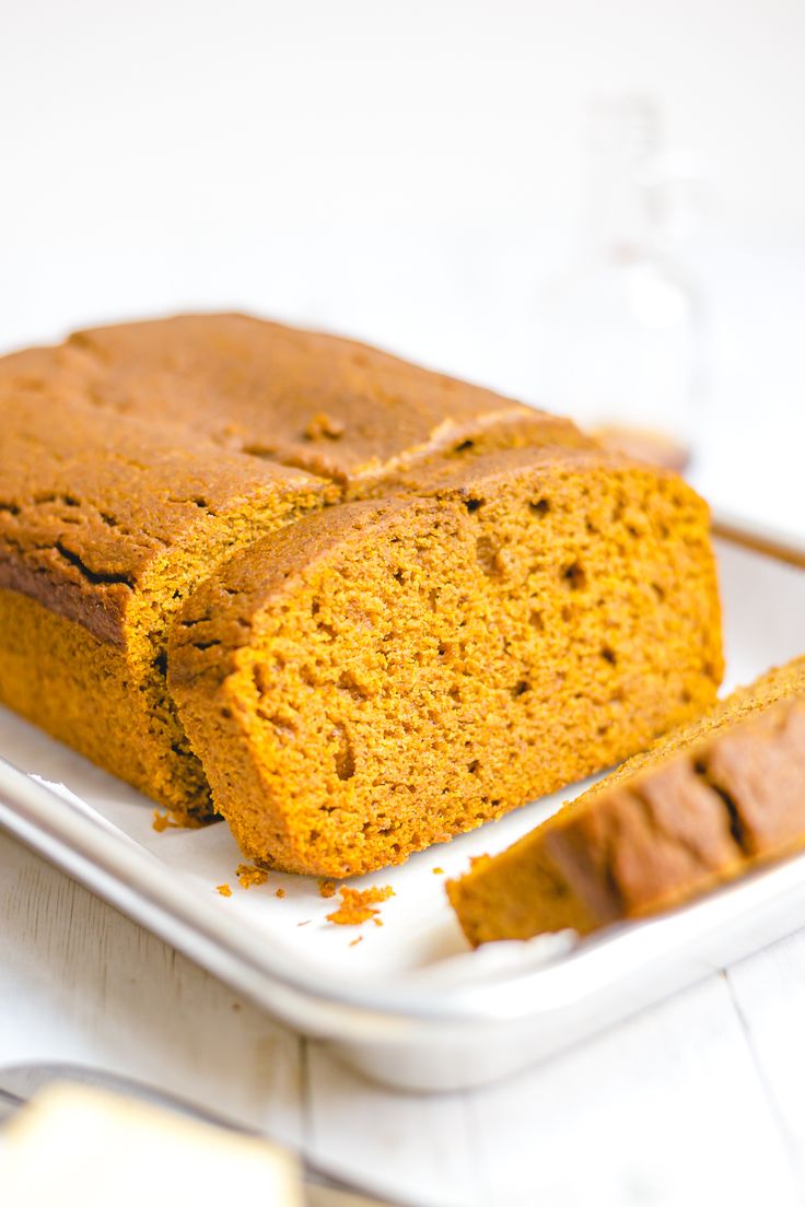 a loaf of pumpkin bread on a white plate with two slices cut off the side