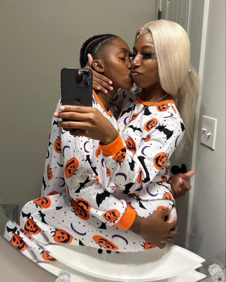 two women in halloween pajamas kissing each other while taking a selfie with their cell phone