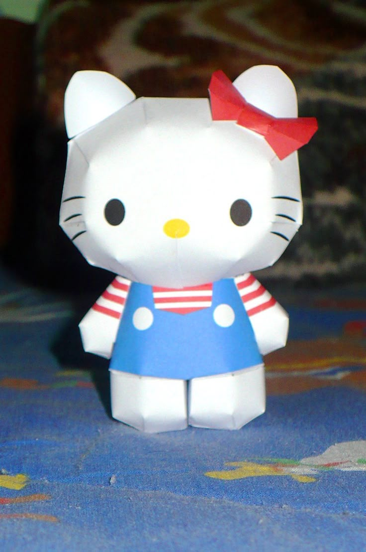 a white hello kitty toy with a red bow on it's head and blue dress