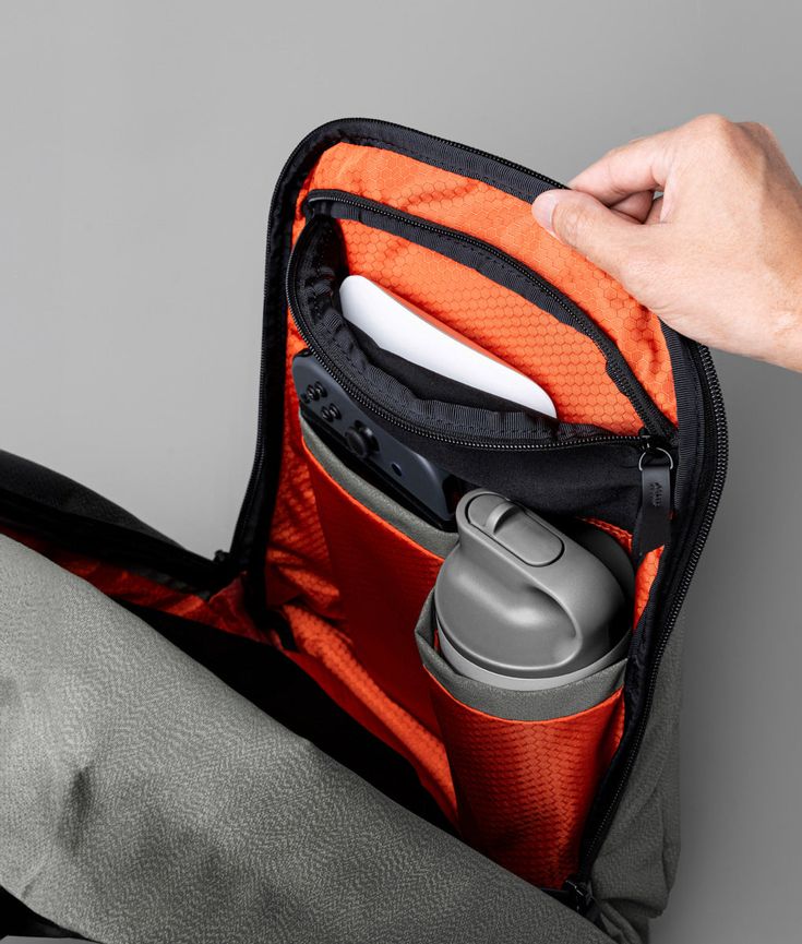 a person holding an orange and black bag with some items in it's pocket