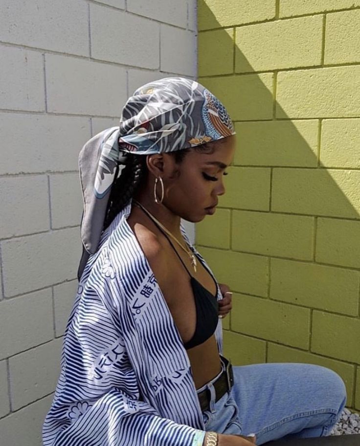 a woman sitting on top of a bench next to a brick wall wearing a head scarf