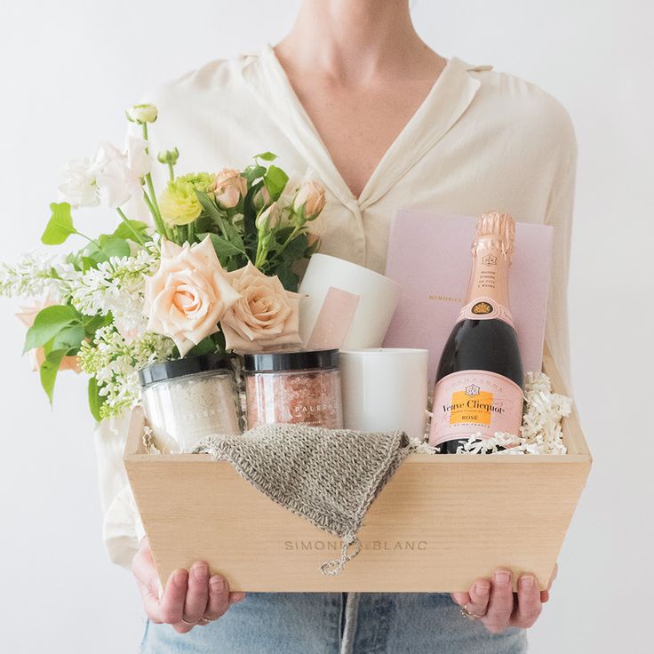 a woman holding a wooden box filled with lots of different types of cosmetics and flowers