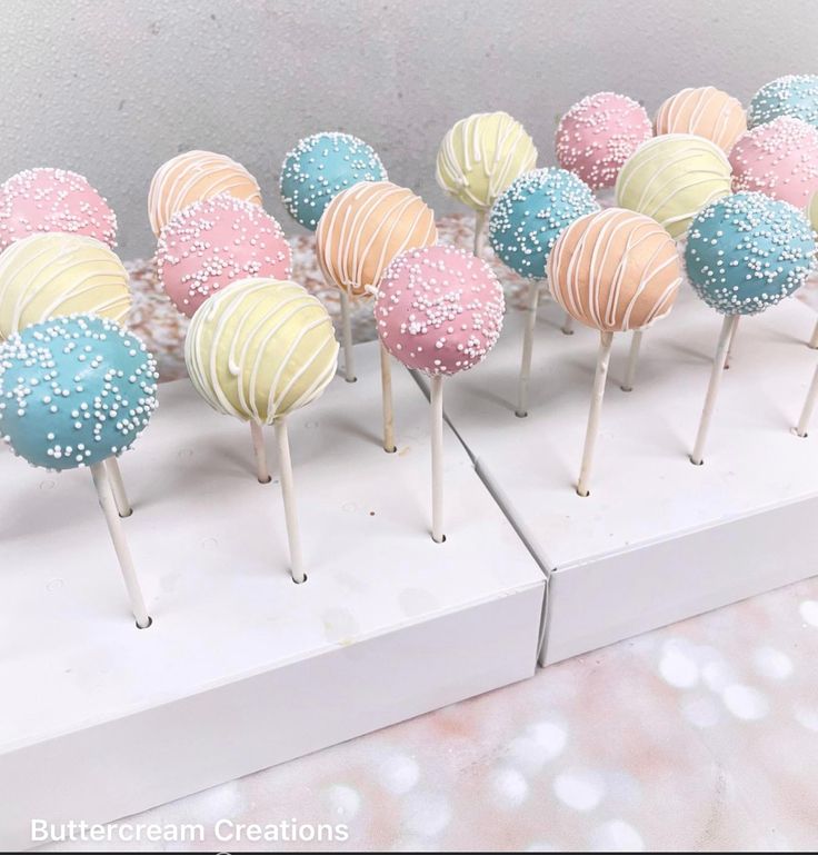 there are many different colored cake pops on the white stand with sprinkles