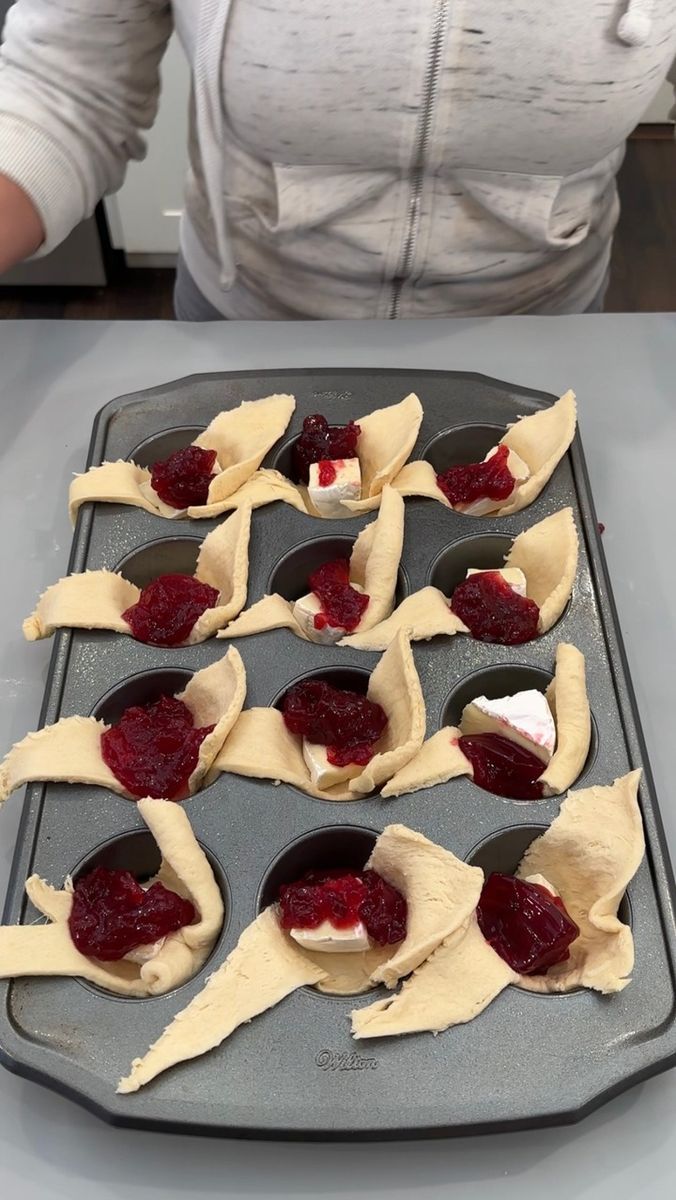 the woman is making pastries on the baking tray with raspberry sauce in them