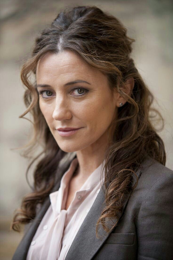 a woman with long hair wearing a suit and white shirt is looking at the camera