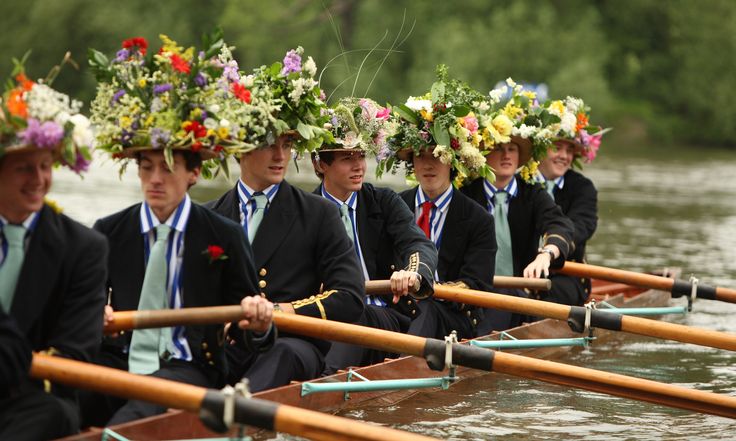 a group of men in suits and hats rowing on a boat with flowers on their heads